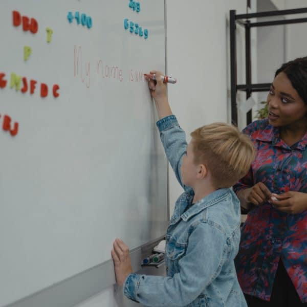 Female teacher instructing male student in writing on white board