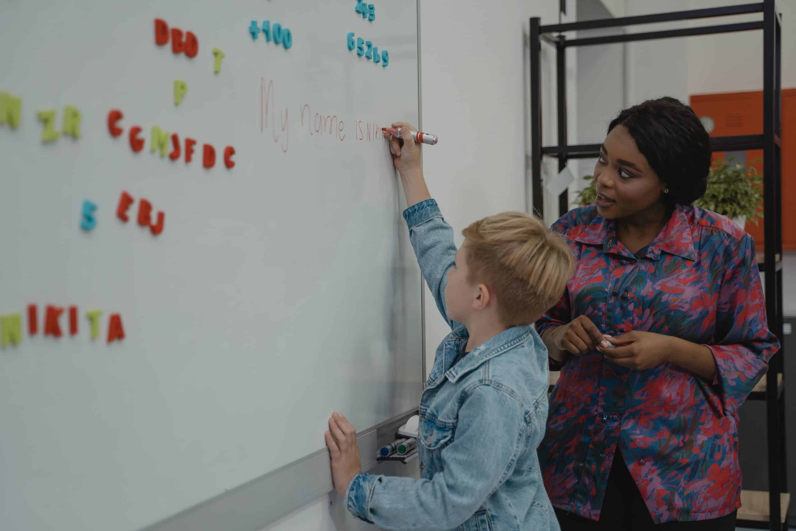 Female teacher instructing male student in writing on white board